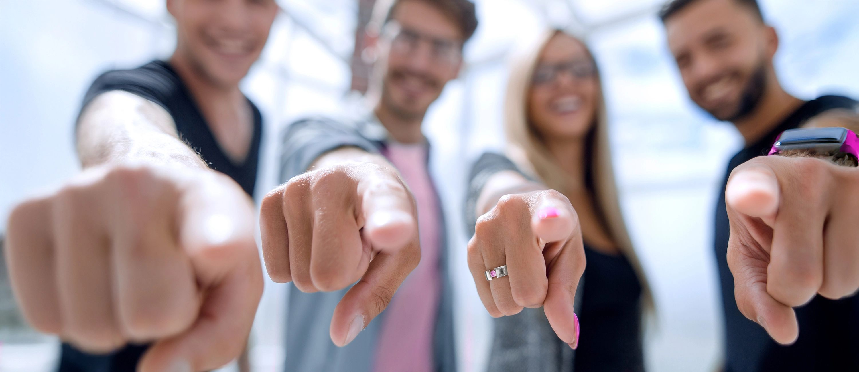 Vier lächelnde Personen zeigen mit dem Finger direkt auf den Betrachter.