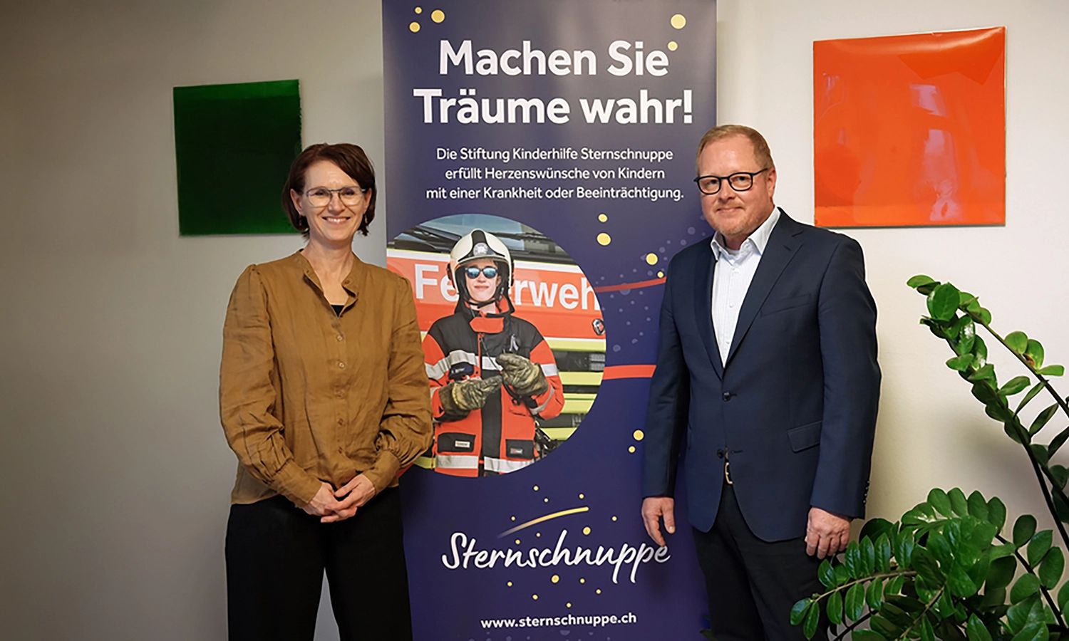 Eine Frau und Heiko Schaffner, CEO ACTIWARE Schweiz GmbH, stehen lächelnd nebeneinander vor einem Banner der Stiftung Kinderhilfe Sternschnuppe. Das Banner trägt die Aufschrift "Machen Sie Träume wahr!