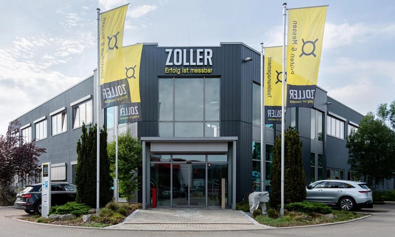 Firmengebäude von e‑zoller mit Fahnen und Eingang – moderner Unternehmenssitz für Präzisionsmesstechnik und digitale Werkzeugverwaltung.