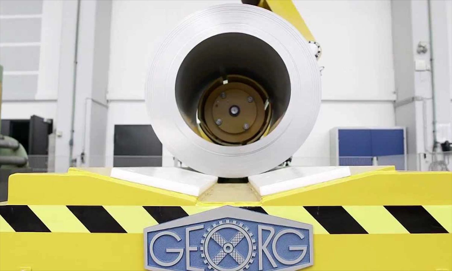 Walzentechnologie von Heinrich Georg – große Metallrolle auf gelber Maschinenvorrichtung mit Firmenlogo, Symbol für Präzision, Engineering und industrielle Fertigungskompetenz.