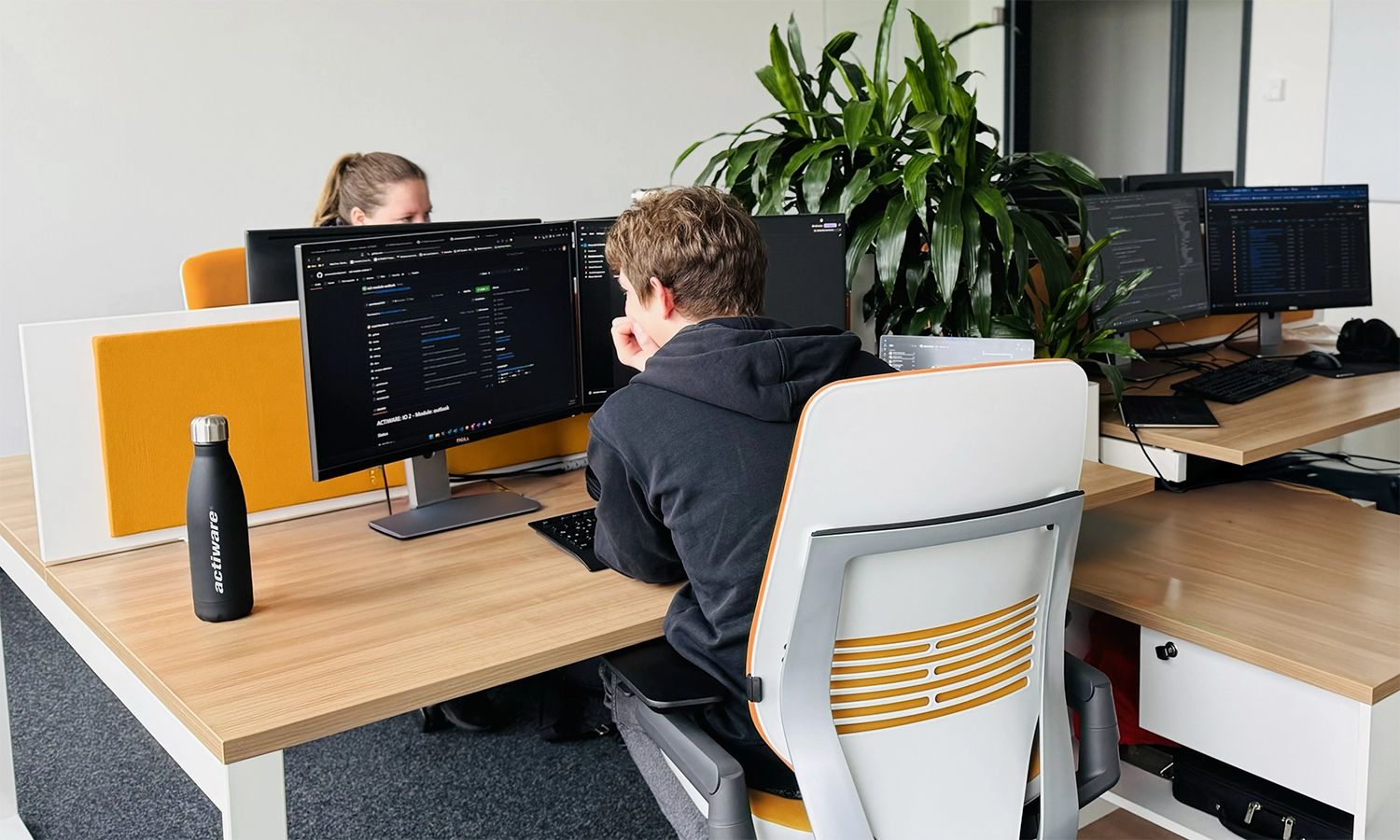 Zwei ACTIWARE Mitarbeitende sitzen an ihren Schreibtischen vor ihren Monitoren