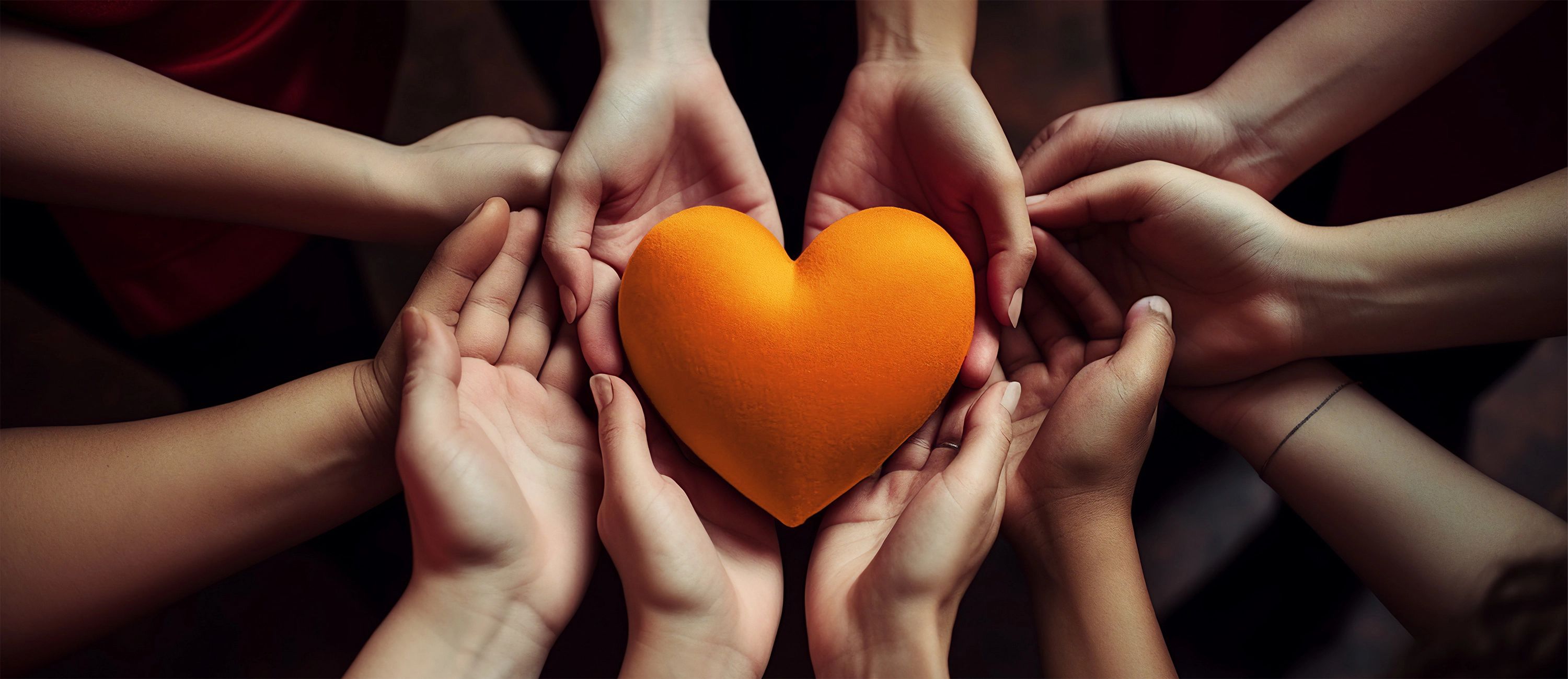 Mehrere Hände halten gemeinsam ein orangenes Herz