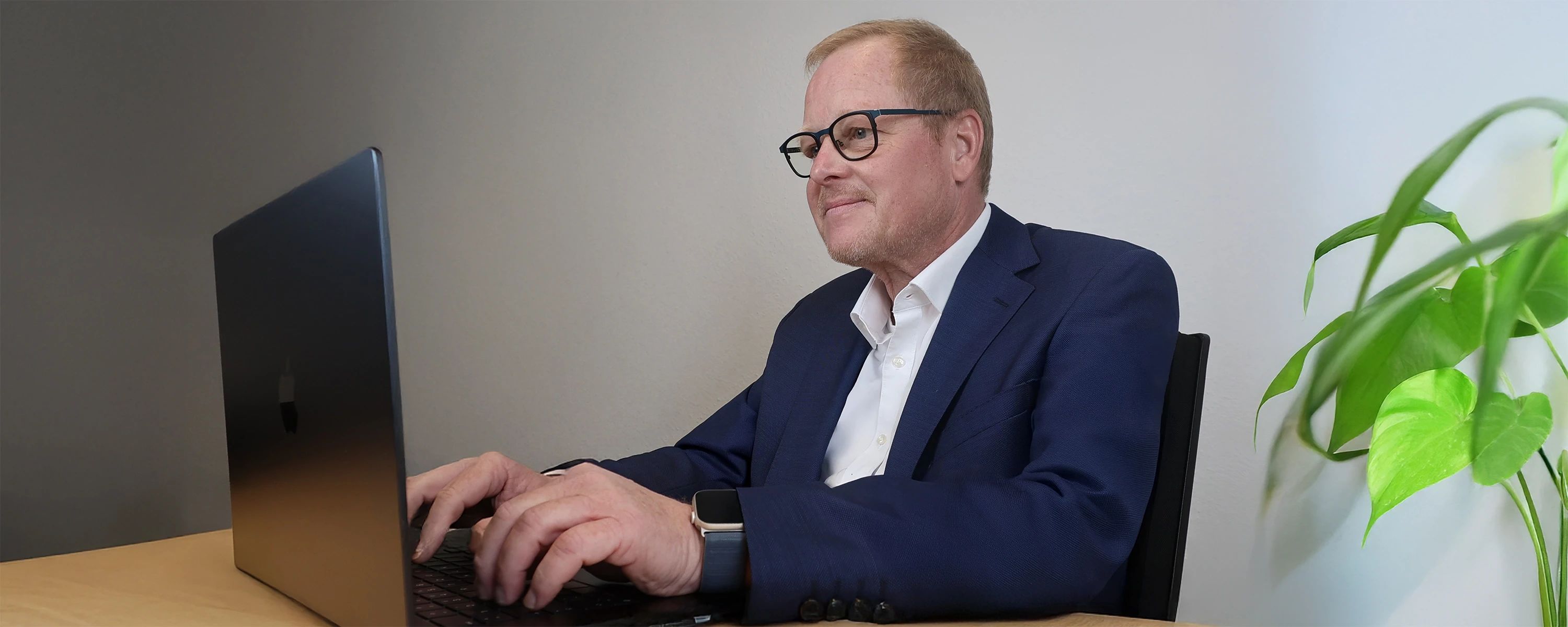 Mann in dunkelblauem Anzug sitzt konzentriert vor Rechner und tippt.