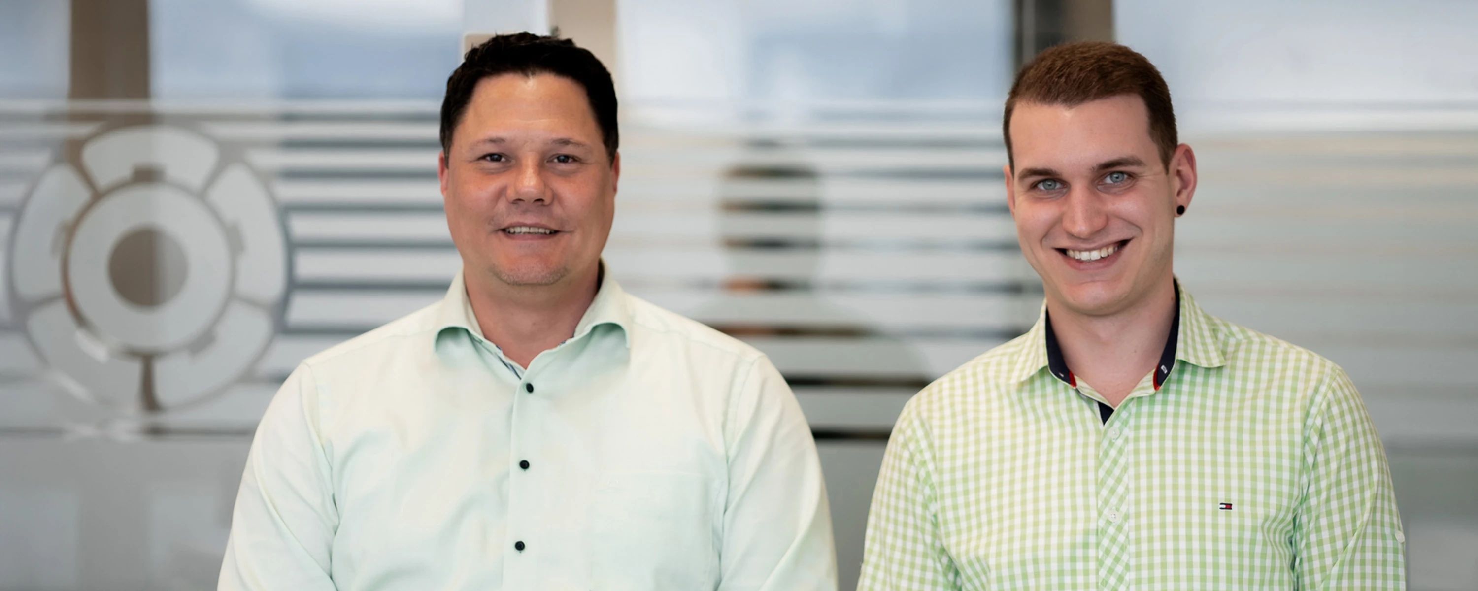 Professionelles Porträtfoto von zwei Männern, die bei Rosenberg Ventilatoren arbeiten, in hellgrünen Hemden, die nebeneinander stehen und freundlich in die Kamera lächeln.