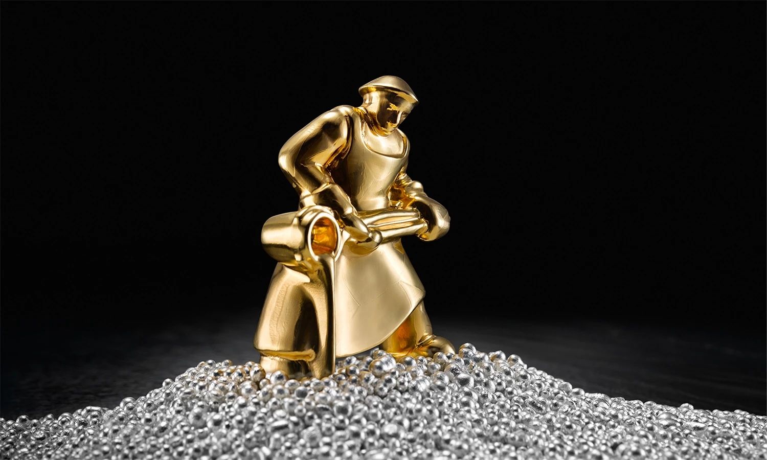 Goldene Figur eines Gießers auf einem Haufen aus Silbergranulat – Symbol der Heimerle + Meule GmbH für Edelmetallverarbeitung, Präzision und traditionelle Handwerkskunst.