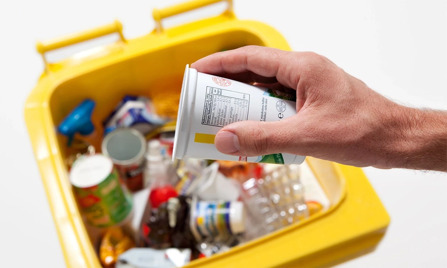 Hand wirft Verpackung in gelbe Tonne – Symbol für Recycling, Abfalltrennung und nachhaltiges Ressourcenmanagement durch Reclay.