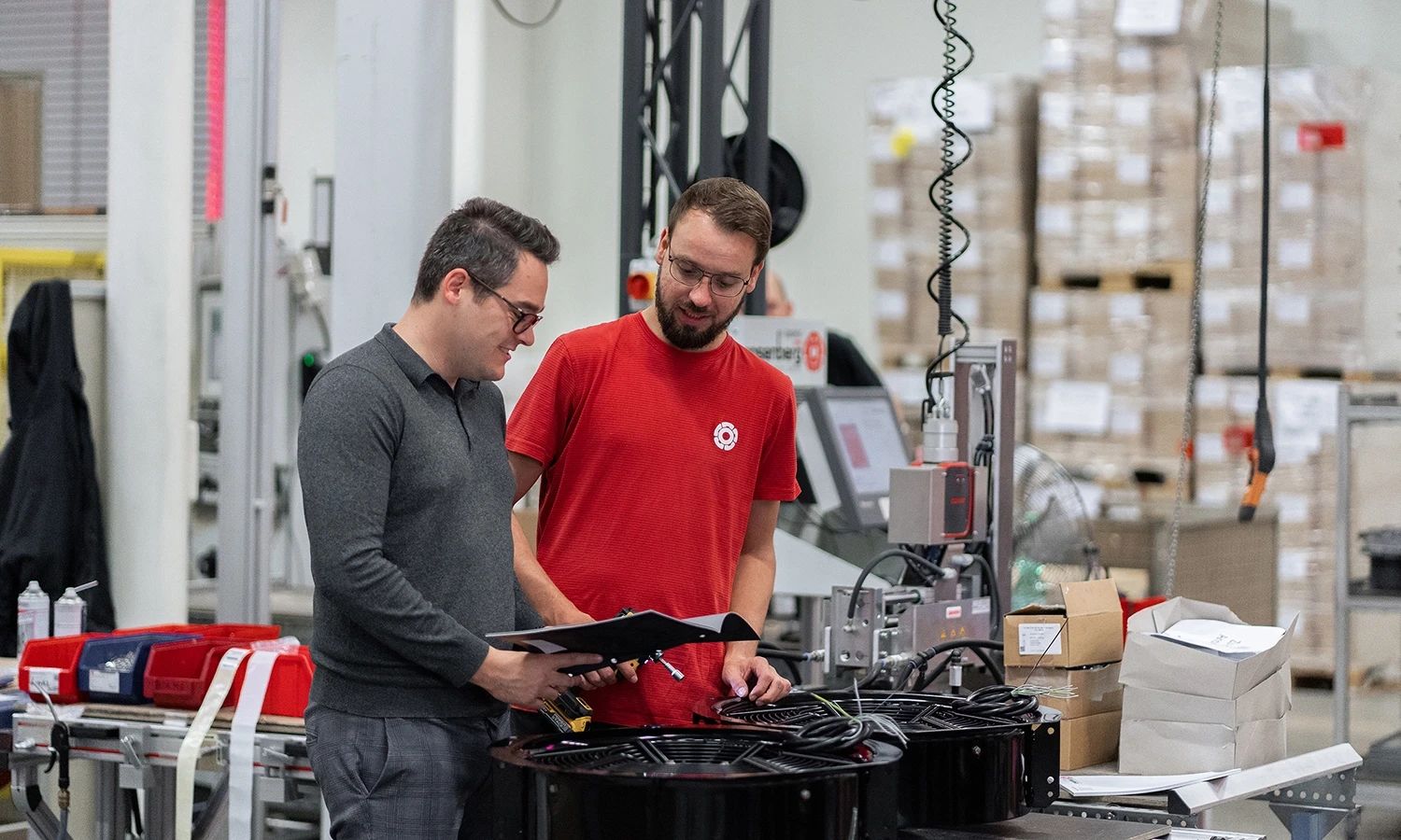 Zwei Rosenberg‑Mitarbeiter in der Produktion stimmen sich über technische Unterlagen ab – Qualitätsprüfung und Fertigung von Lüftungs‑ und Klimatechnikkomponenten.