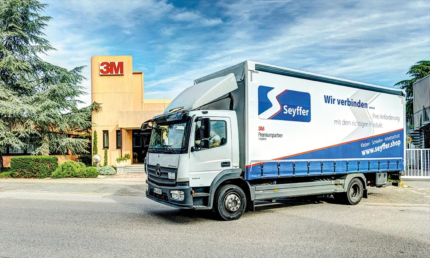 Seyffer‑LKW vor einem Firmengebäude – Transportfahrzeug mit Firmenlogo und Slogan ‚Wir verbinden …‘, Partnerunternehmen im Bereich Klebe‑ und Verbindungstechnik.