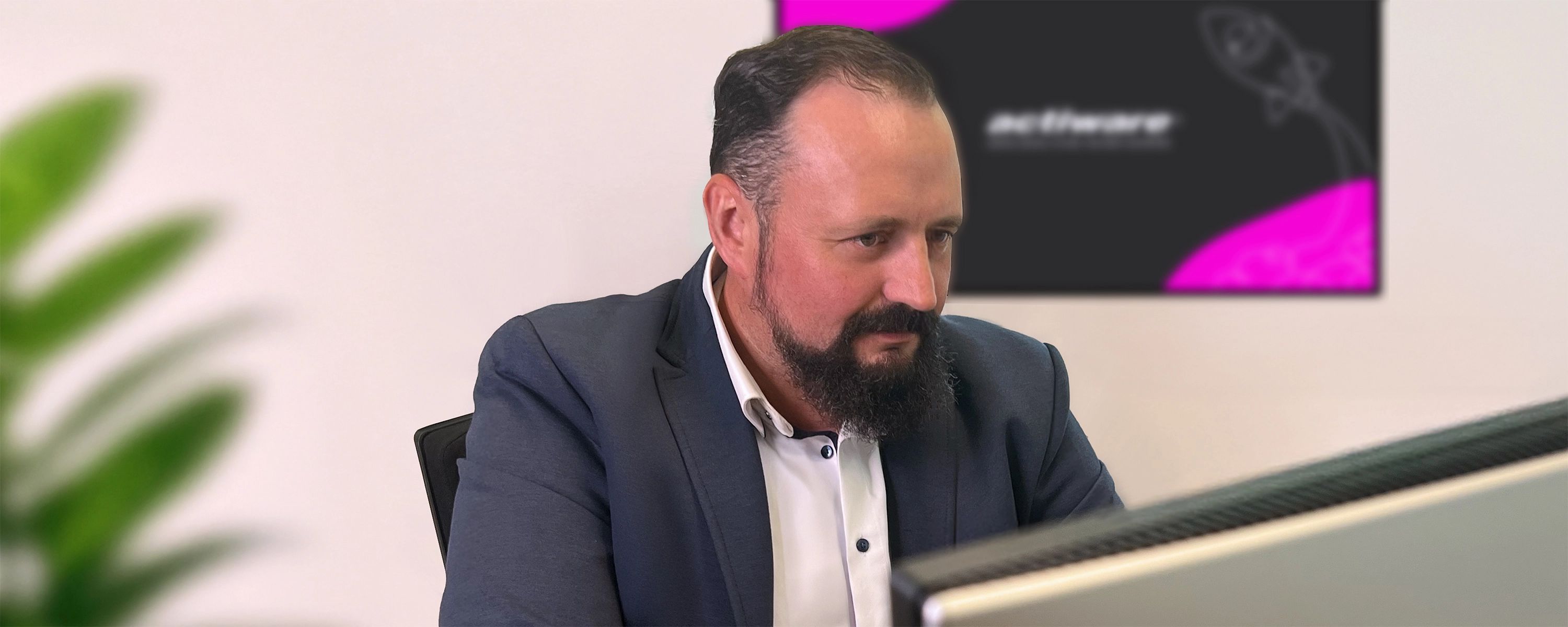 Ein Mitarbeiter schaut konzentriert auf seinen Monitor, im Hintergrund hängt ein weiterer Bildschirm mit dem ACTIWARE-Desktop-Hintergrund.