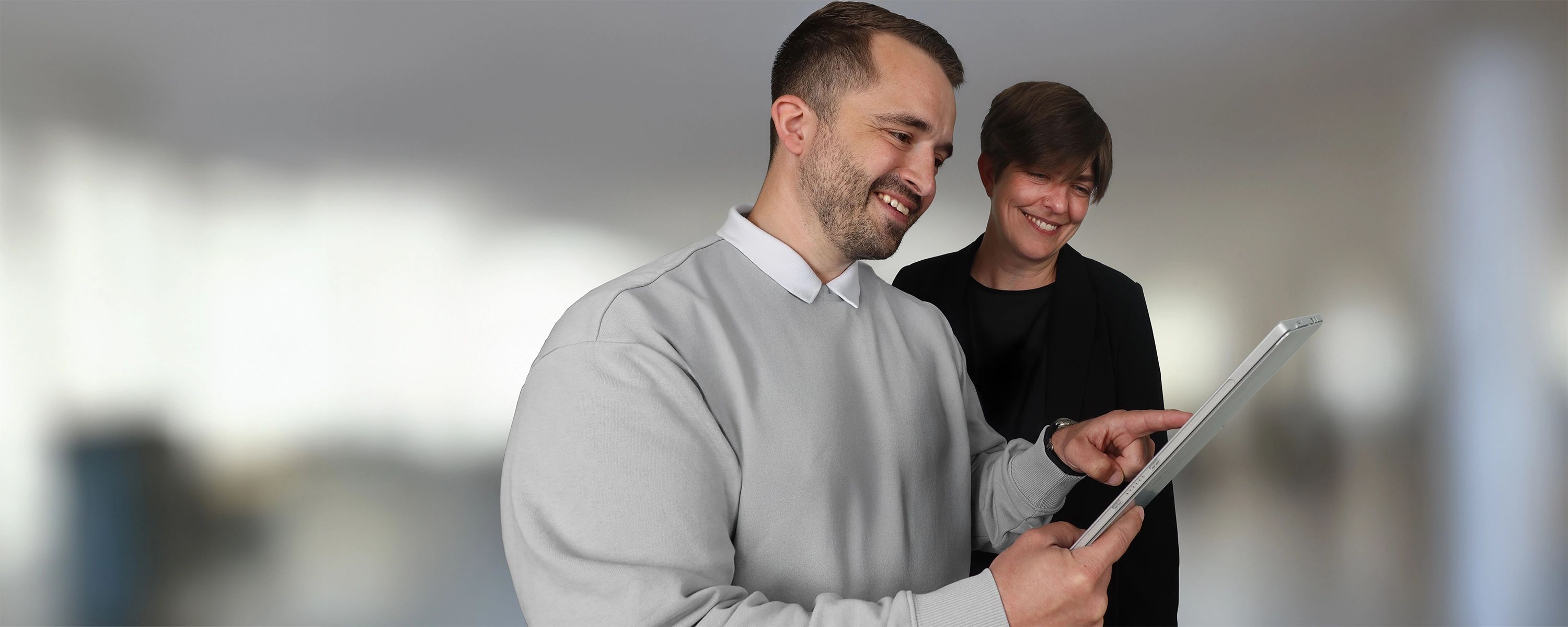 Zwei Mitarbeitende stehen nebeneinander und schauen auf ein Tablet, einer zeigt mit dem Finger darauf.