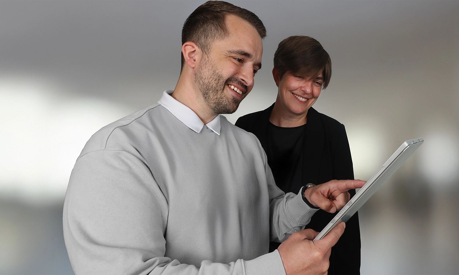 Zwei Mitarbeitende stehen nebeneinander und schauen auf ein Tablet, einer zeigt mit dem Finger darauf.