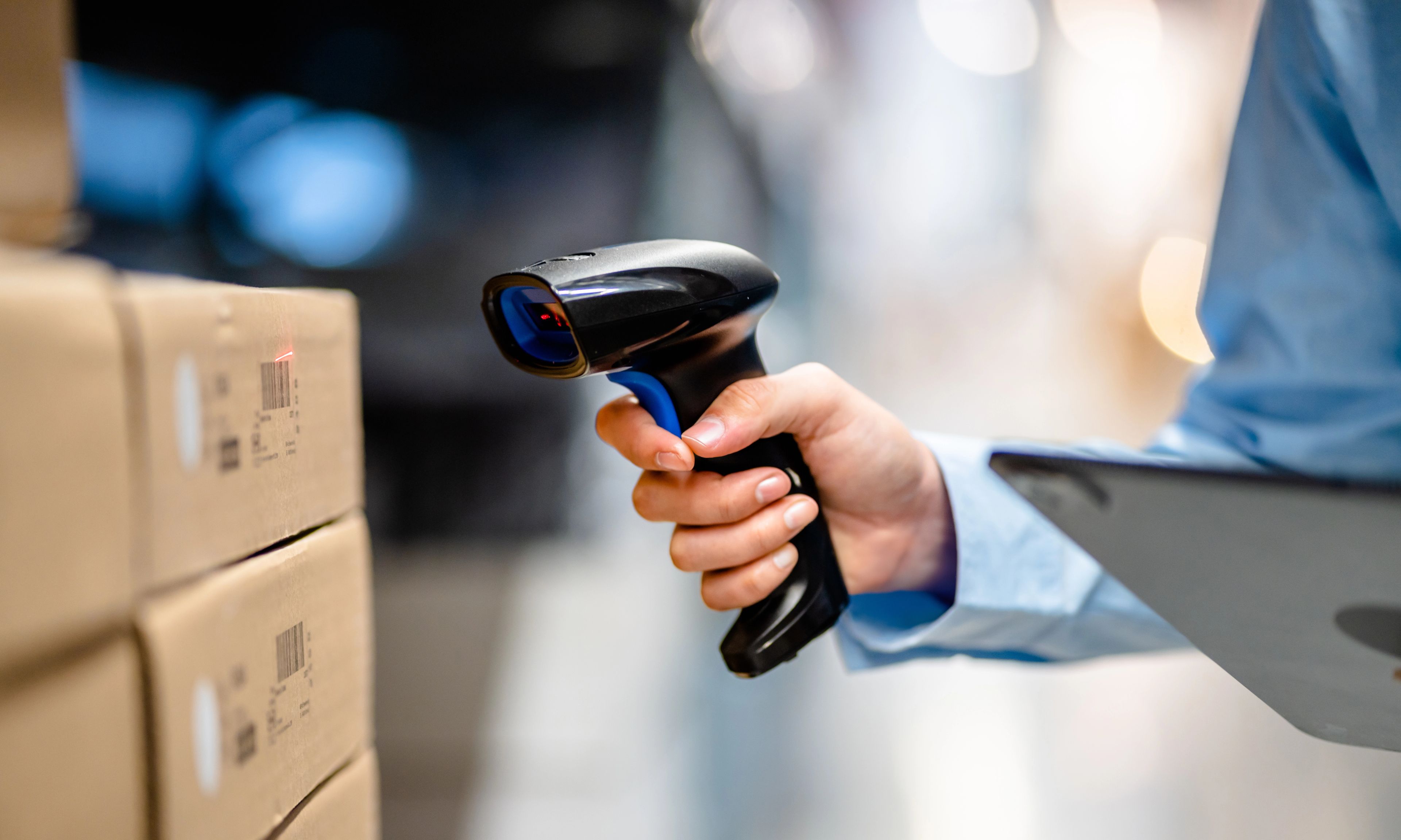 Mitarbeiter*in scannt mit einem Handscanner Barcodes auf Kartons im Lager.