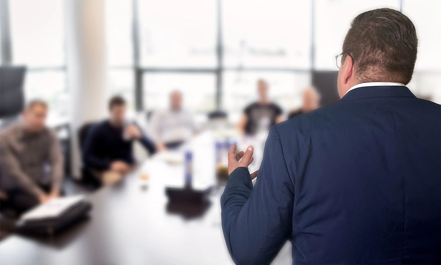 Trainer hält Präsentation vor einer Gruppe von Teilnehmenden in einem Besprechungsraum.