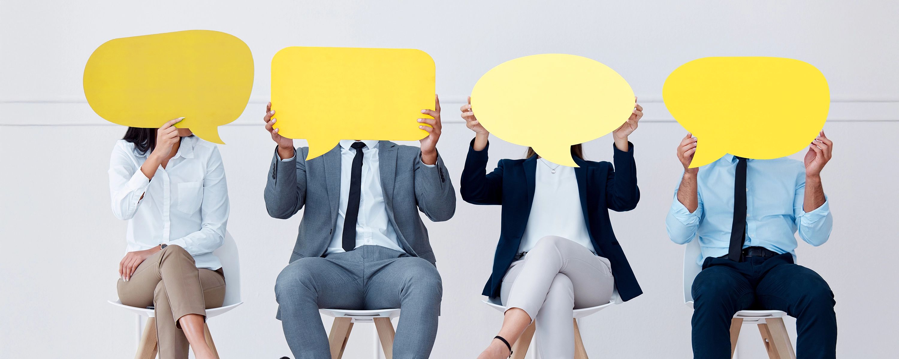 Vier Personen in Business‑Kleidung halten gelbe Sprechblasen vor das Gesicht – symbolisches Headerbild für Kundenmeinungen und Referenzen auf der Website.