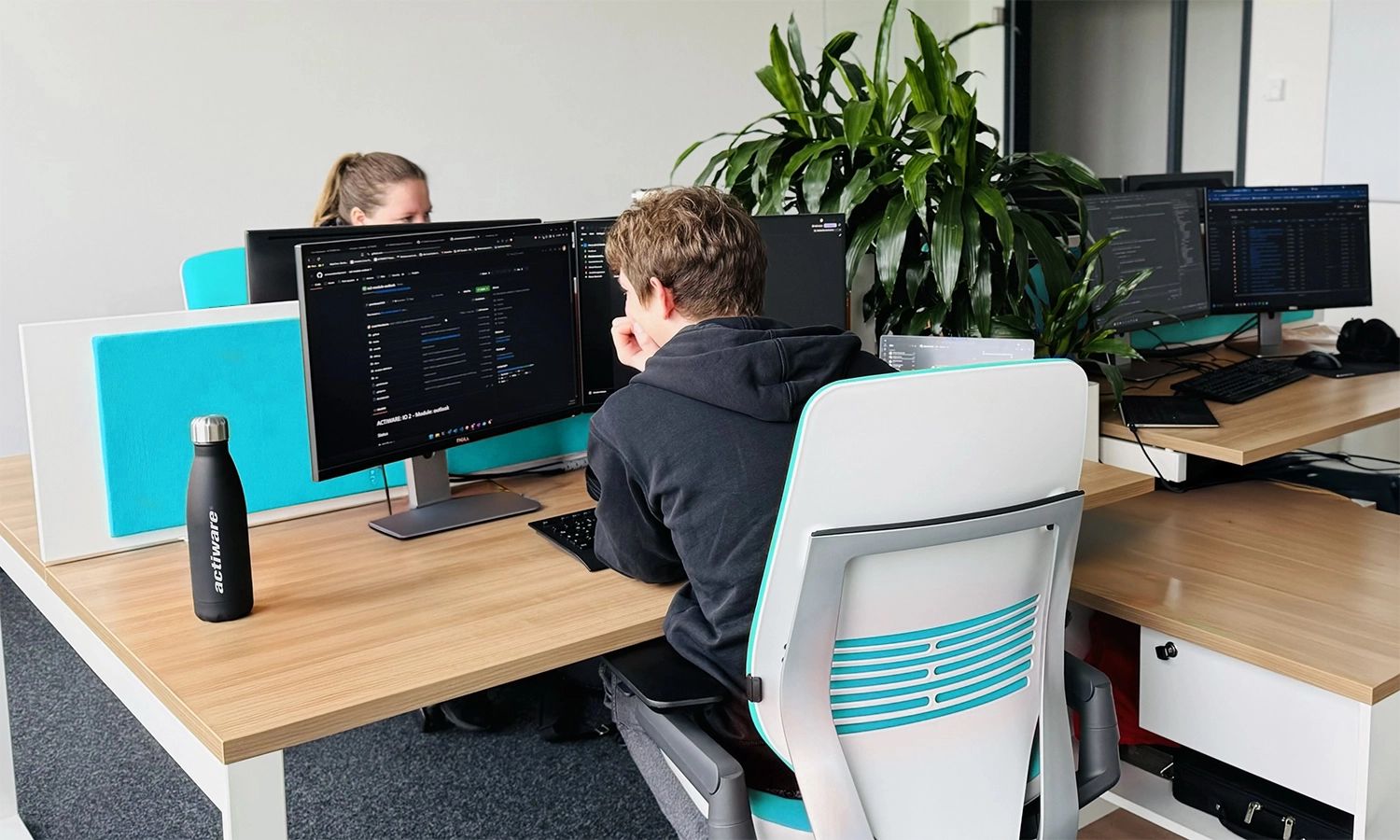 Zwei ACTIWARE Mitarbeitende sitzen an ihren Schreibtischen vor ihren Monitoren.