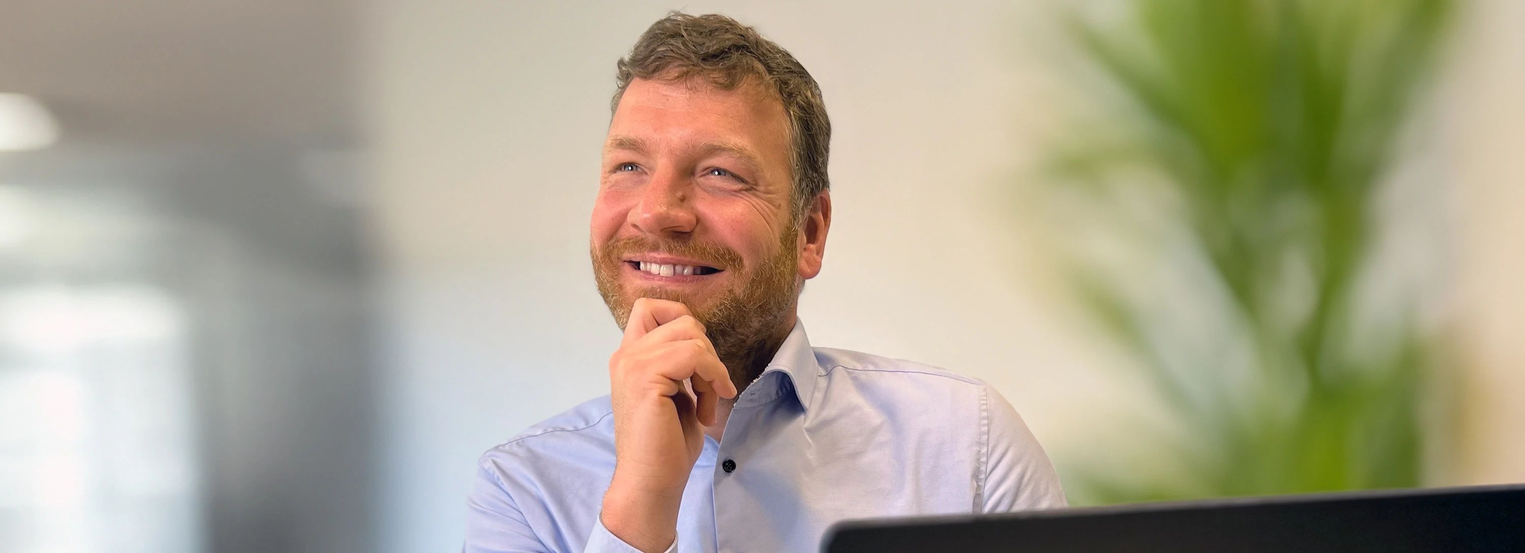 Porträt eines lächelnden Mitarbeiters, der nachdenklich nach oben schaut und seine Hand am Kinn hat.