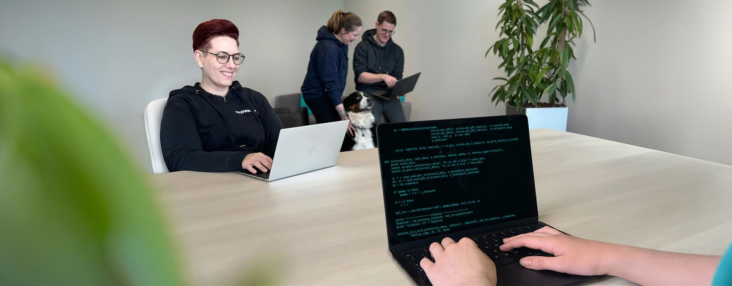 Personen arbeiten in einer modernen Büroumgebung mit Laptops und einem Hund.