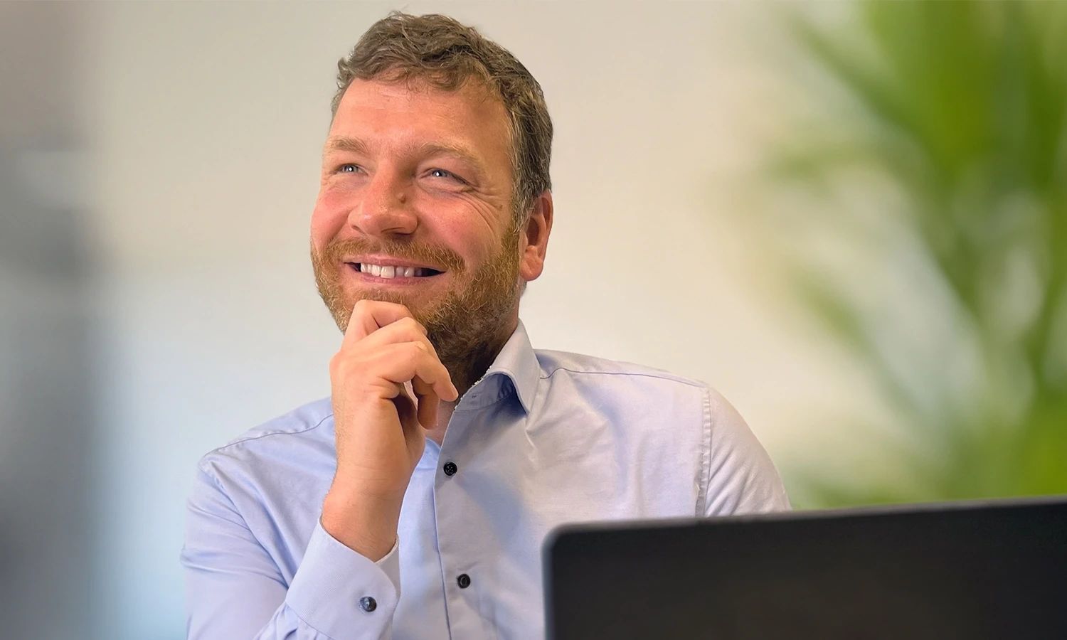 Porträt eines lächelnden Mitarbeiters, der nachdenklich nach oben schaut und seine Hand am Kinn hat.