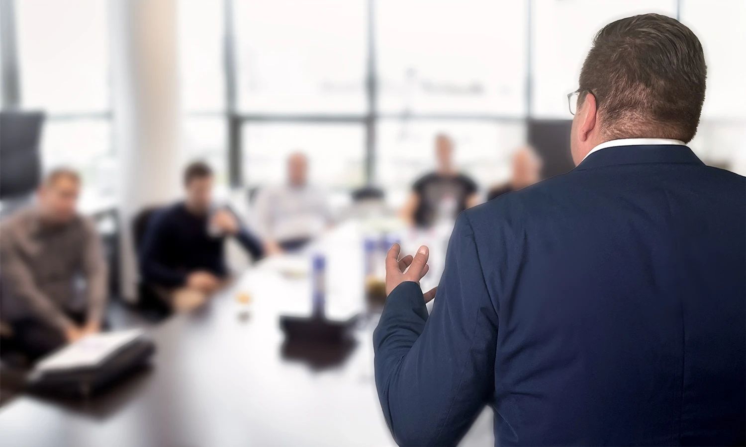 Trainer hält Präsentation vor einer Gruppe von Teilnehmenden in einem Besprechungsraum.