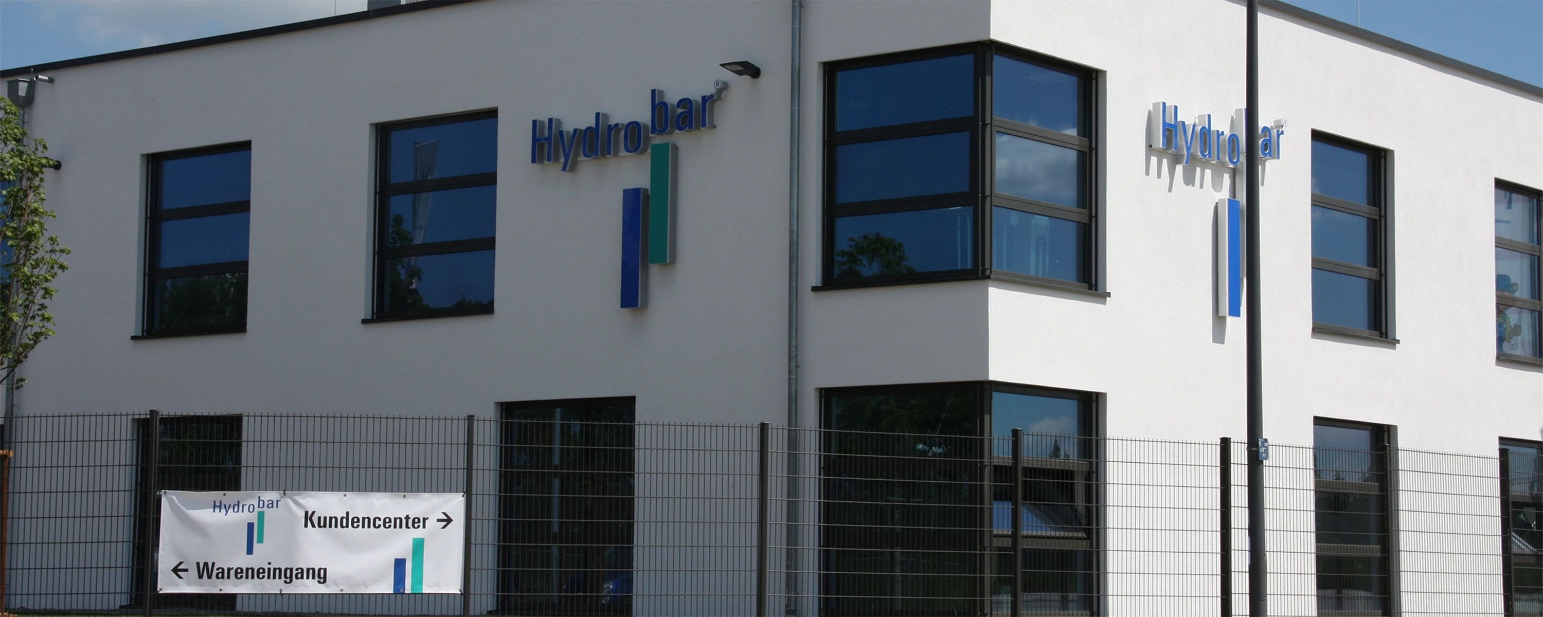 Firmengebäude von HydroBar – modernes Verwaltungs‑ und Servicezentrum für Hydraulik‑ und Pneumatiklösungen mit Beschilderung zum Kundencenter und Wareneingang.